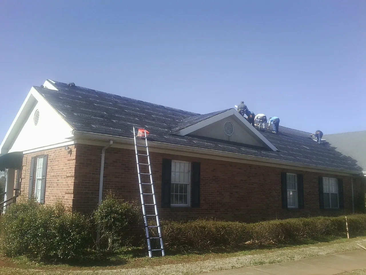 Crew tearing shingles off a brick ranch roof with a ladder set — Emergency Roof Repair work by our crew in Mason